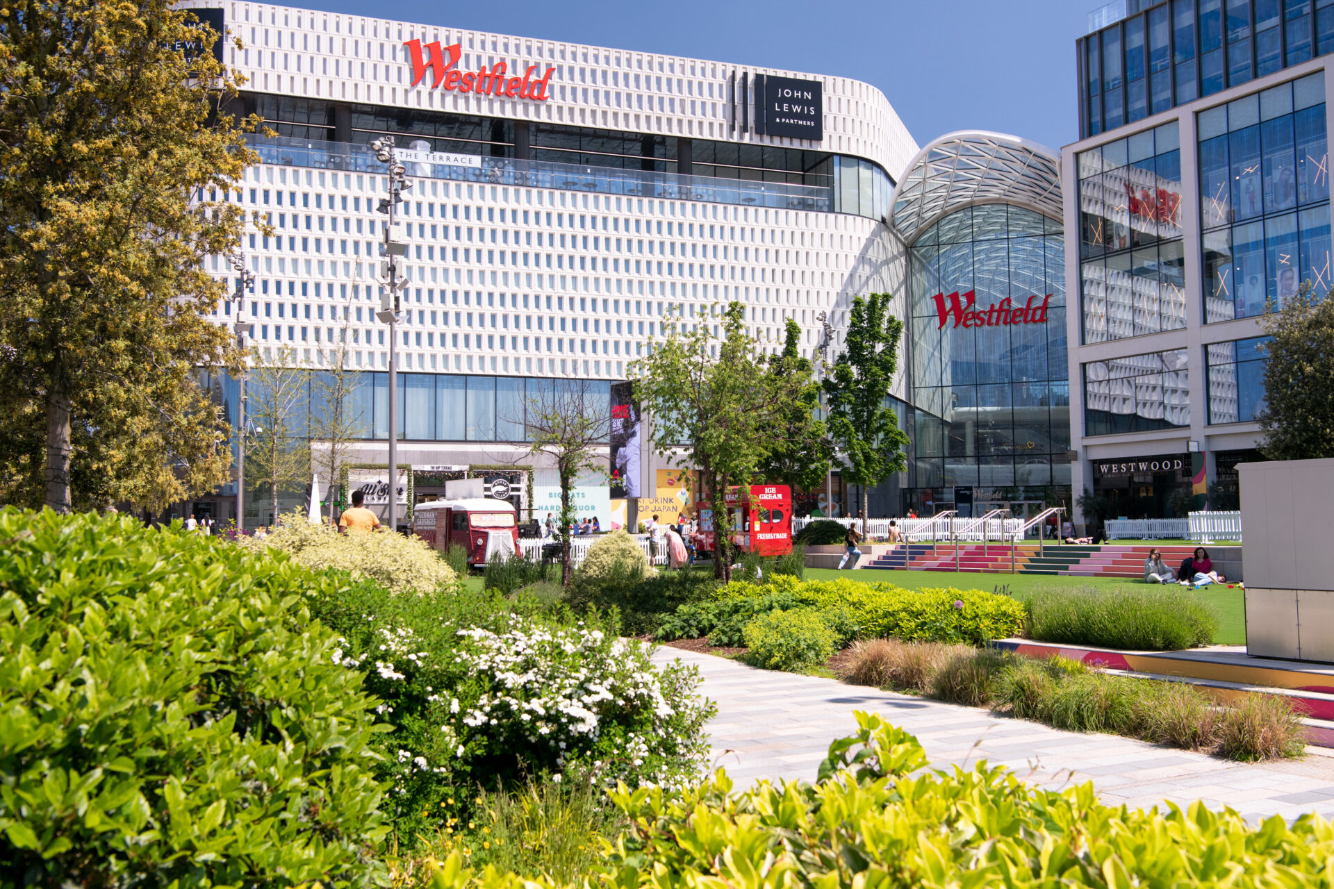 Exterior of a shopping centre bearing the logo 'Westfield' with green space in front