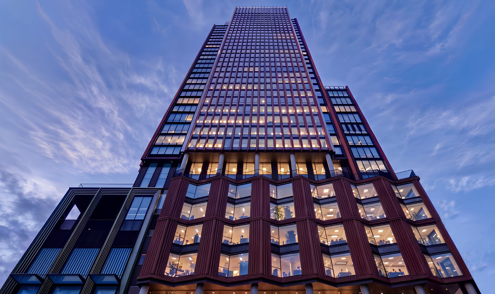View looking up a skyscraper at dusk featuring lots of windows