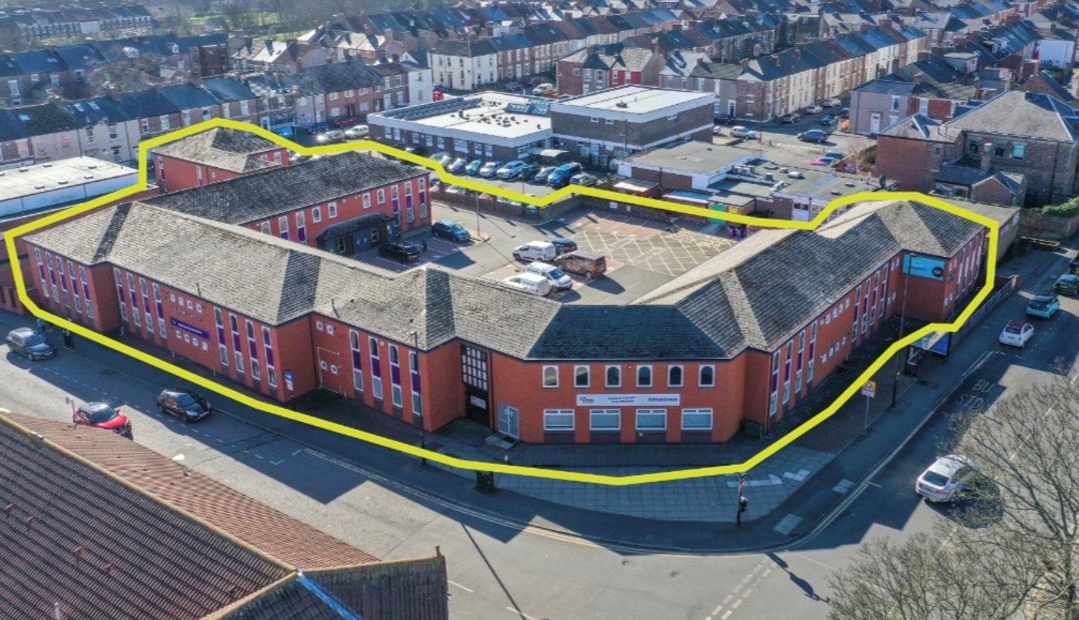 Aerial view of a series of interlinked brick buildings with a yellow line surrounding the site