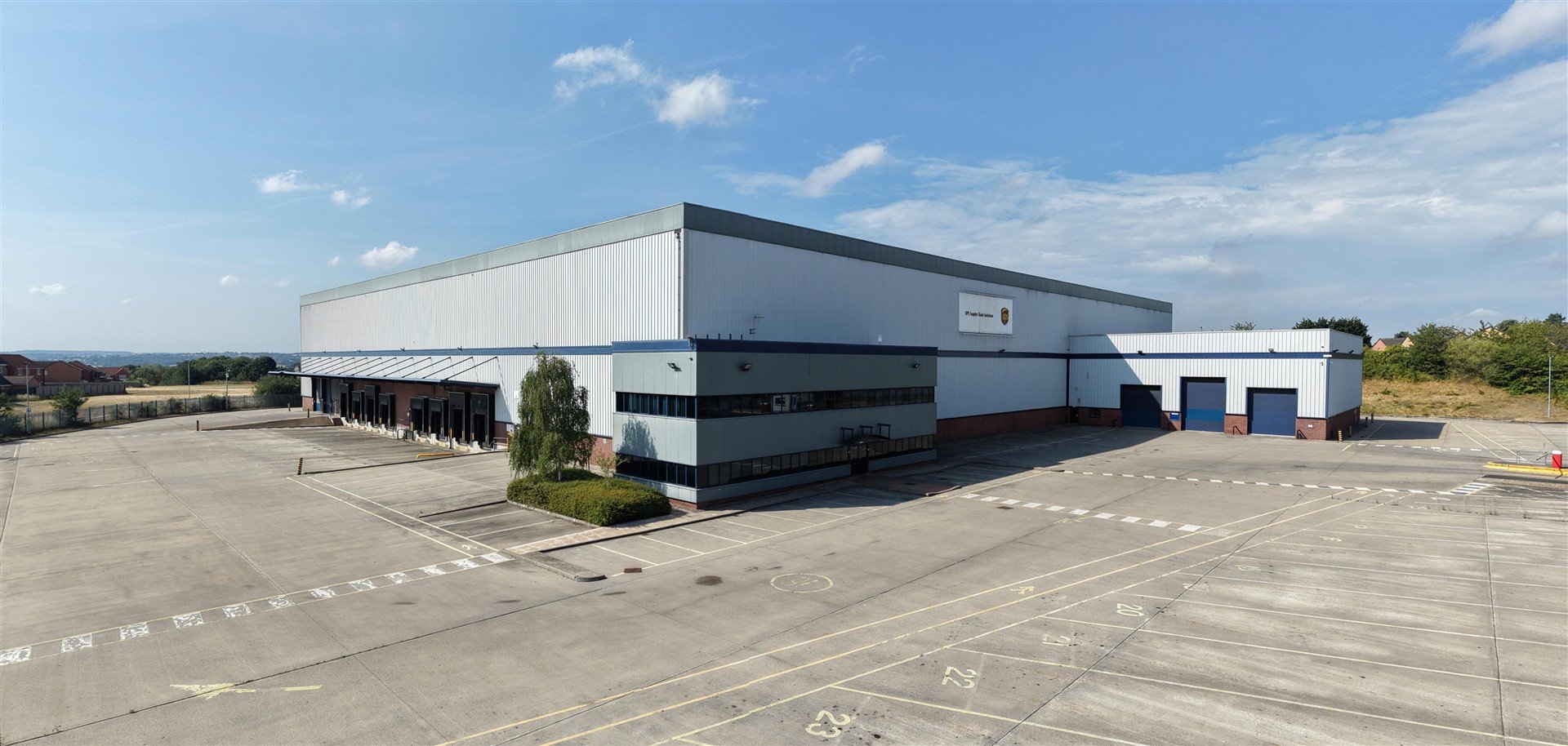 A large industrial building with a card and car parking in front