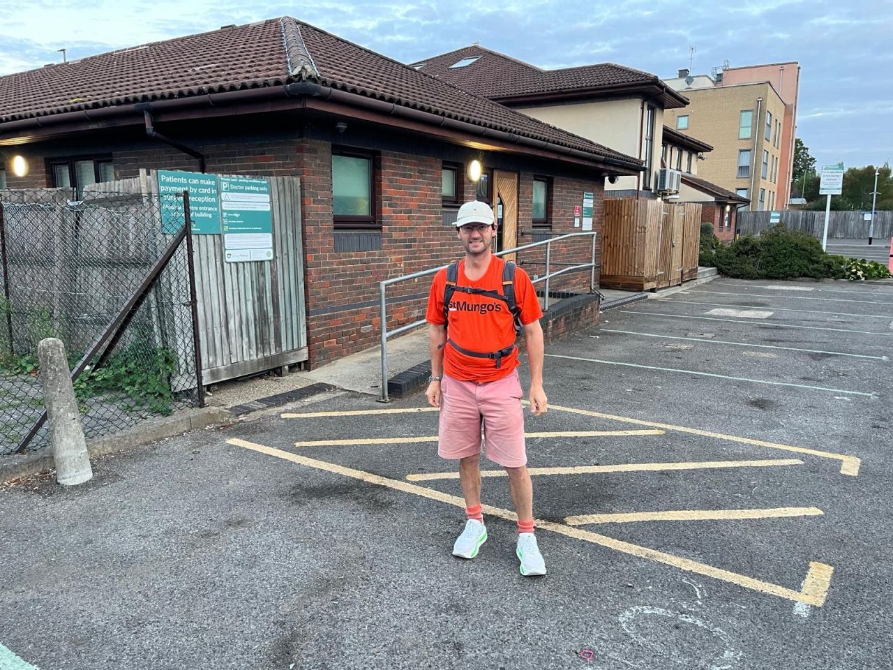 A man wearing shorts, a baseball cap and an orange shirt stood in front of a building