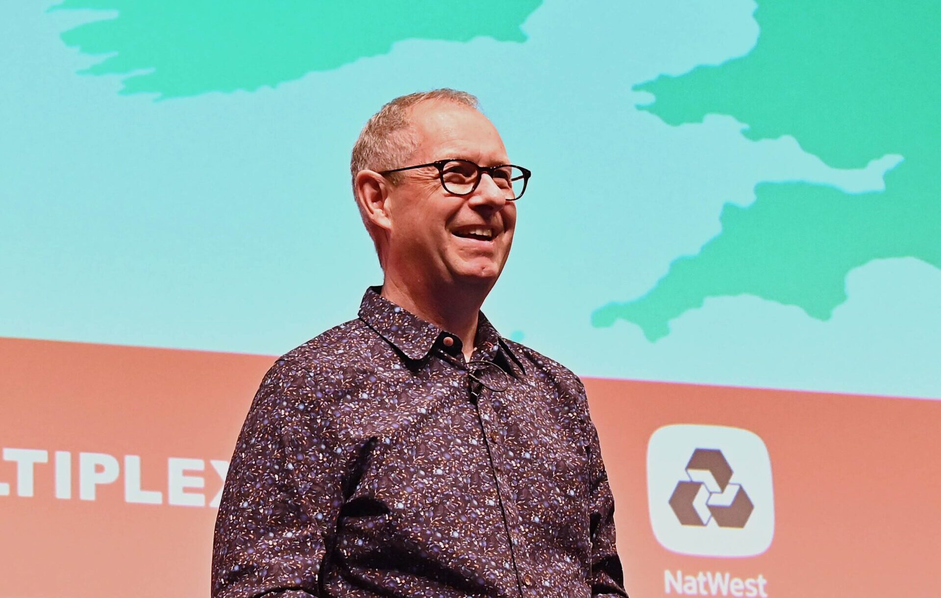 A smiling man stood in front of a large screen