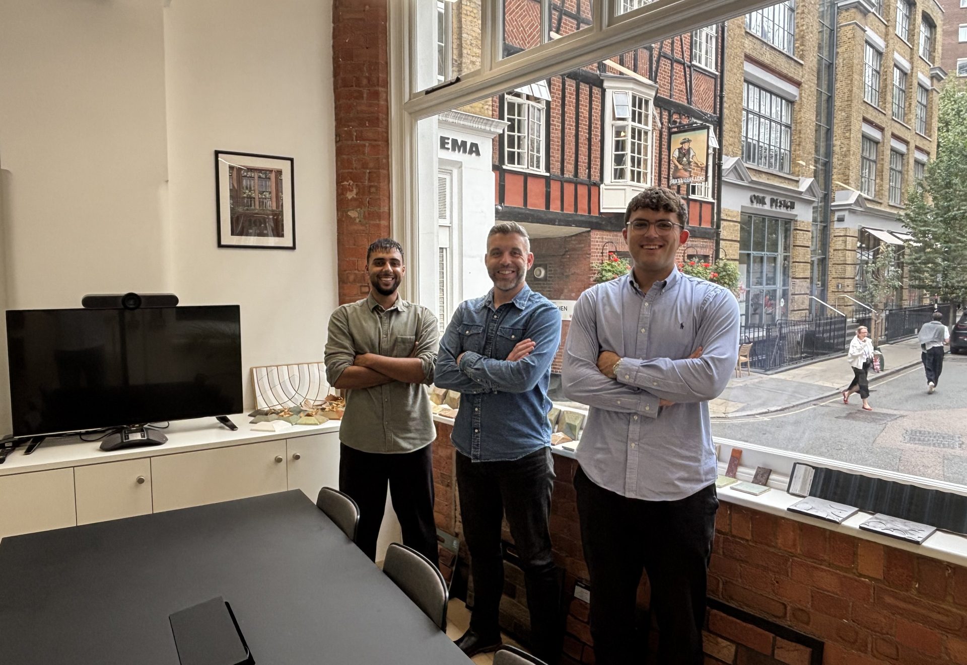 Three men with their arms crossed stood in front of an office window