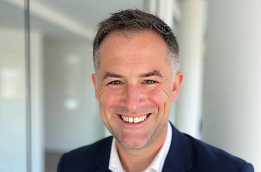 A smiling man wearing a dark suit jacket and white shirt