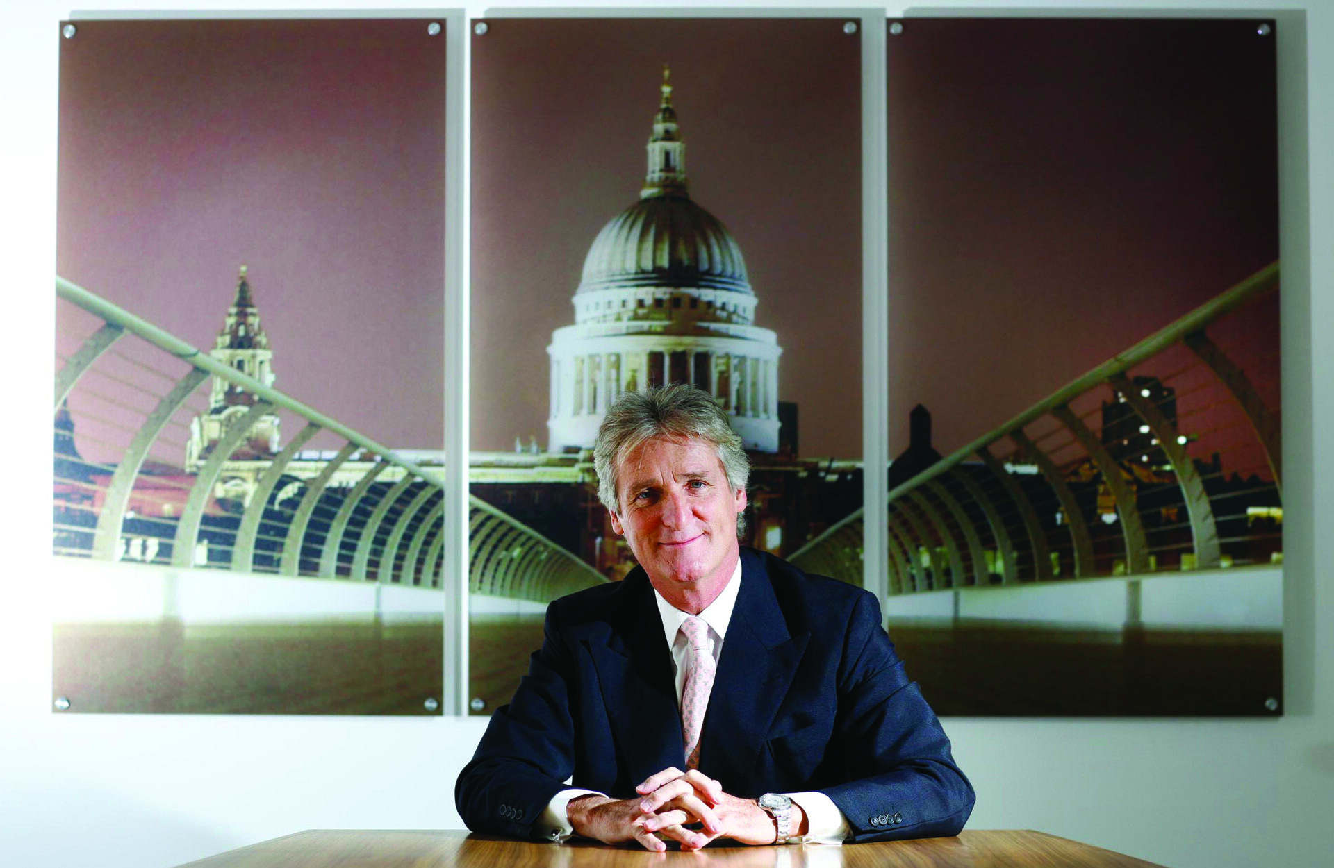 A smiling man sat behind a desk with a picture of St Paul's Cathedral behind him
