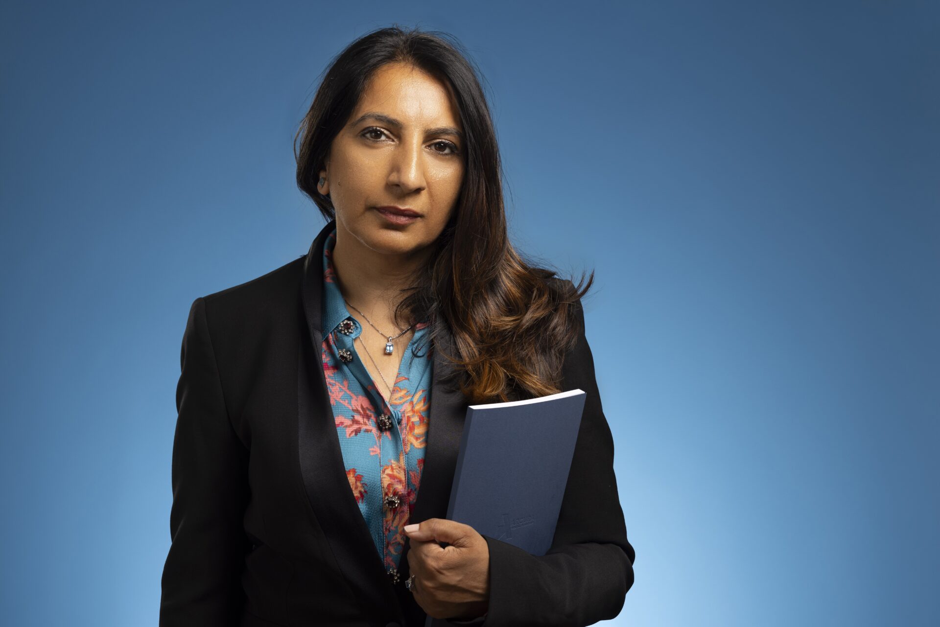 A woman with long dark hair holding a blue book pictured against a blue background