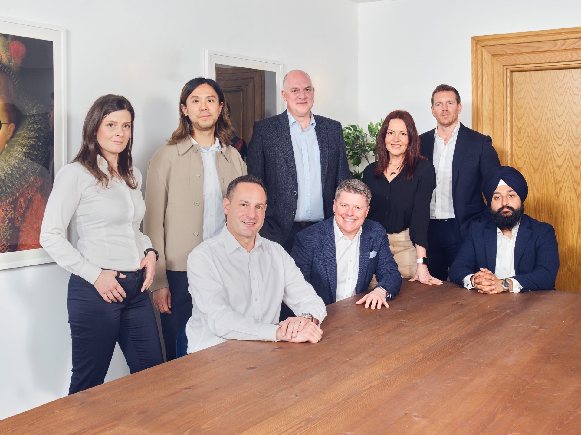 Eight OPRE Group team members pose around a wooden table in an office.