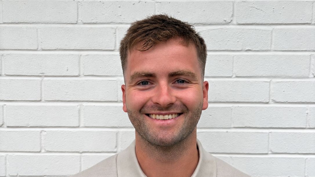 Ben Sykes, senior surveyor at Bruce Gillingham Pollard, smiling in front of a white brick wall
