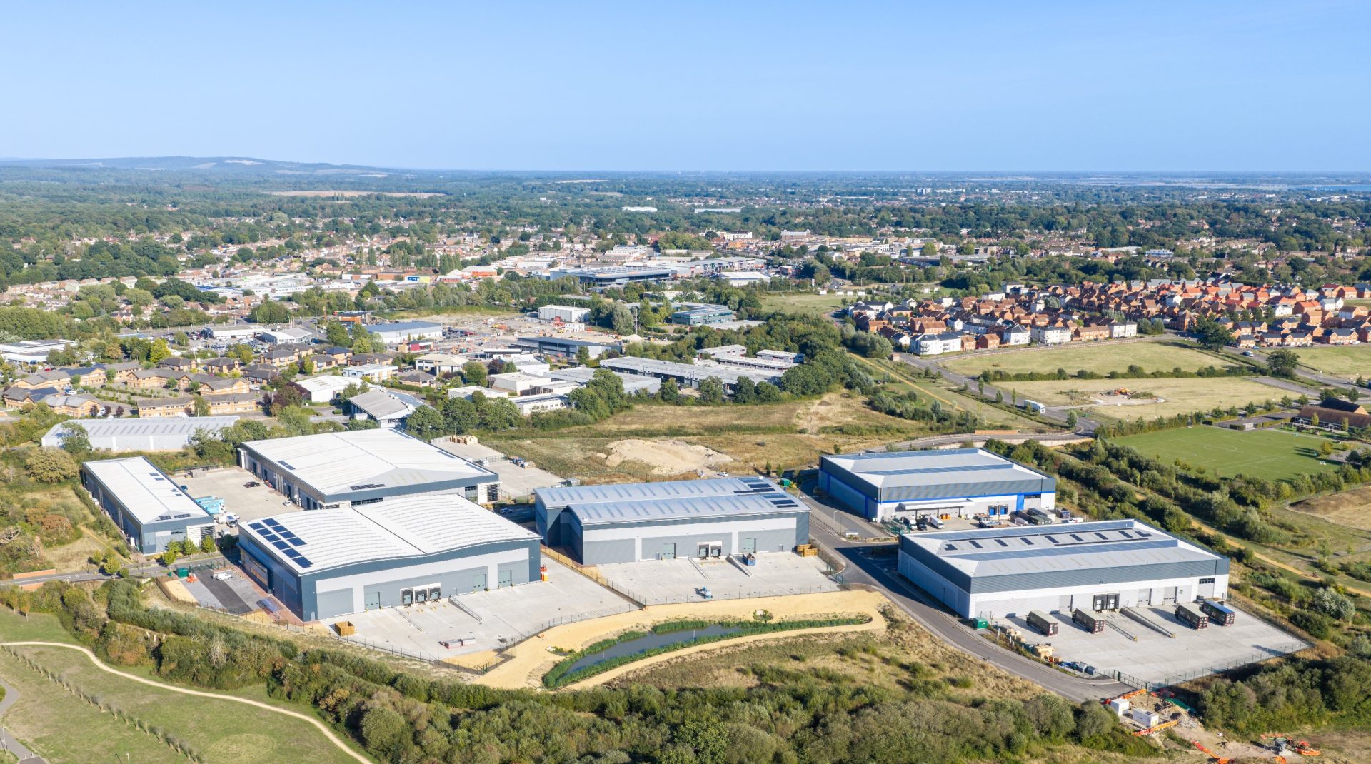 Aerial view of a modern industrial and commercial development beside housing and open fields