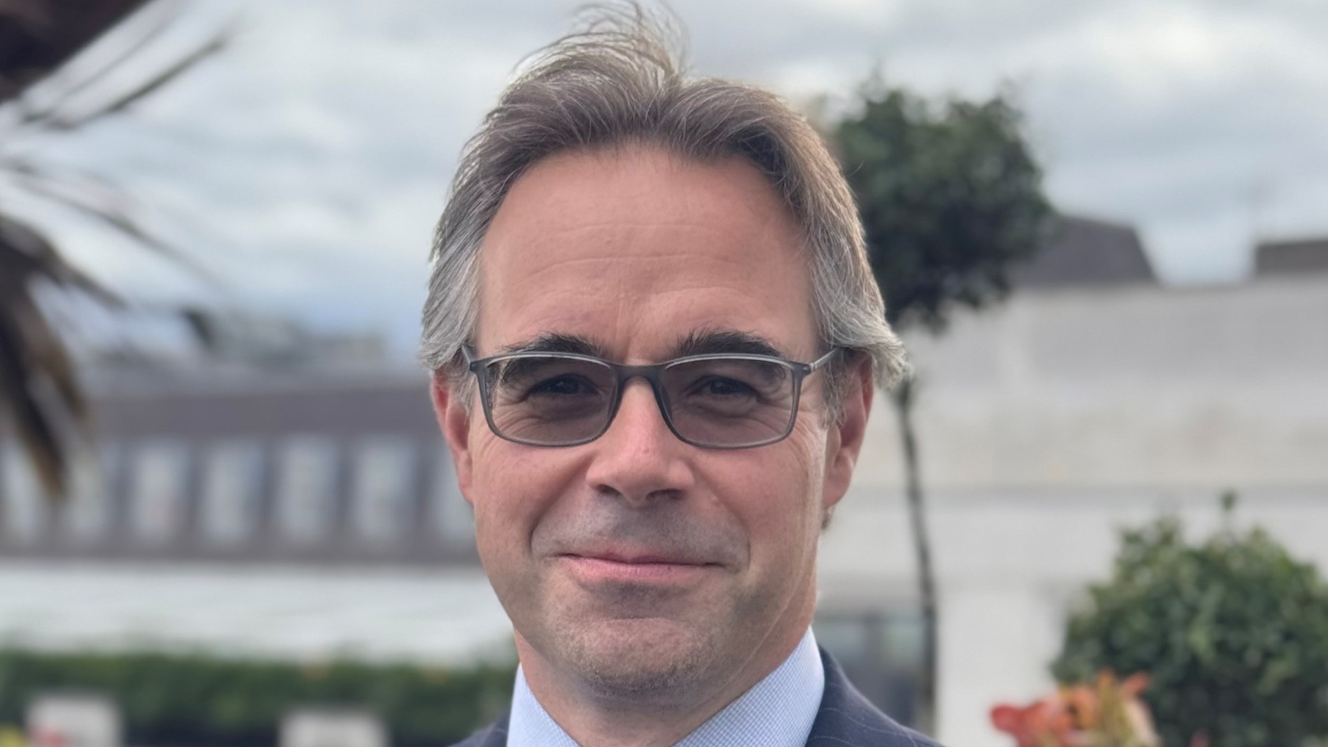 Alex Ayres, Colliers director, wearing a suit and glasses outdoors