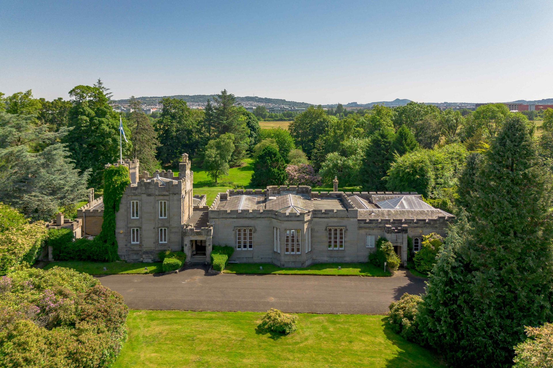 Aerial view of Edinburgh’s historic Millburn Tower, a stone castellated country house surrounded by trees and lawns.