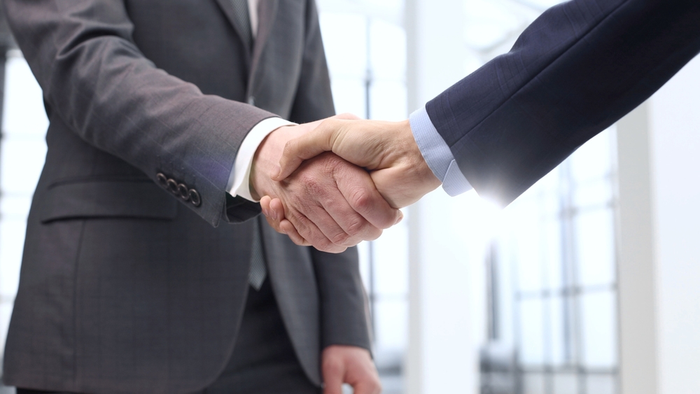 Businesspeople in suits shake hands, symbolizing the deal for two Ramsay private hospitals