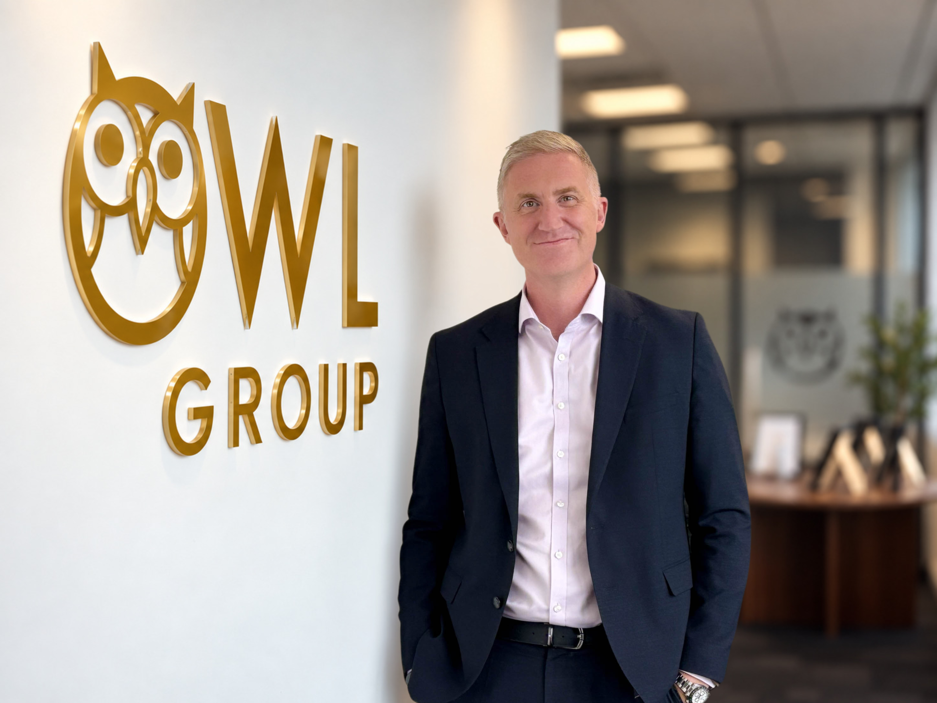 Steve Breslin stands beside an Owl Group logo in a suit.