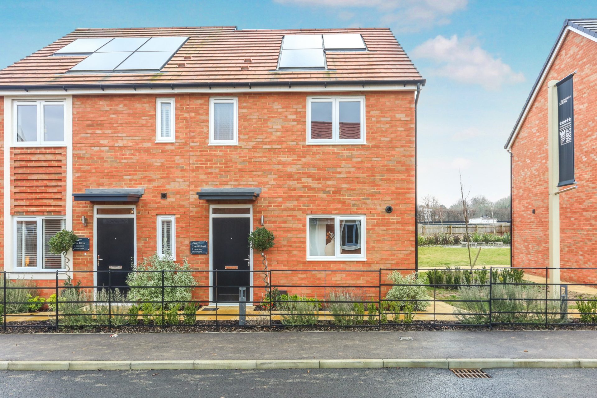 Newly built brick terraced homes with solar panels, front gardens and a paved street
