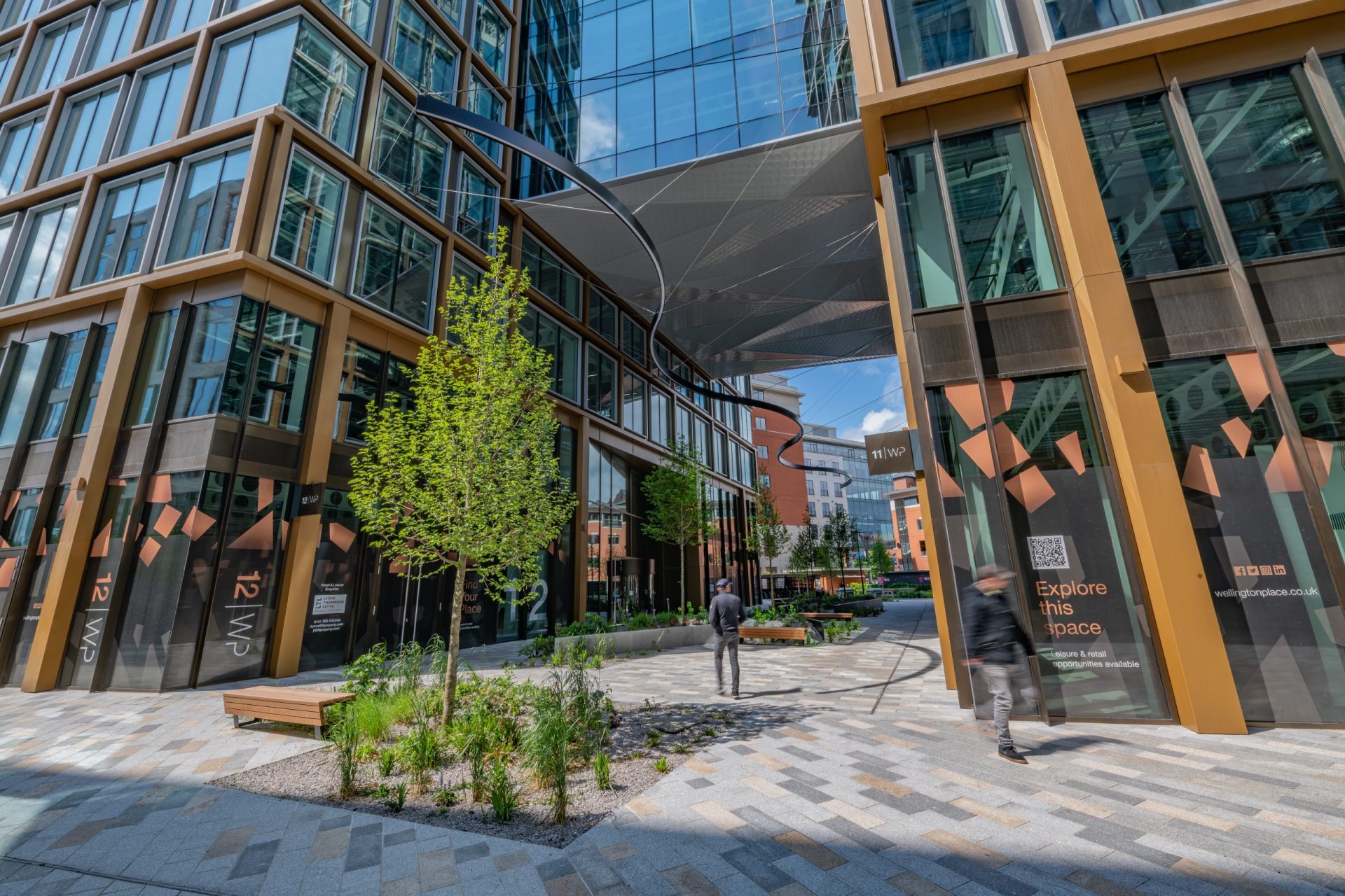 Modern commercial buildings lining a landscaped pedestrian plaza with people walking between offices