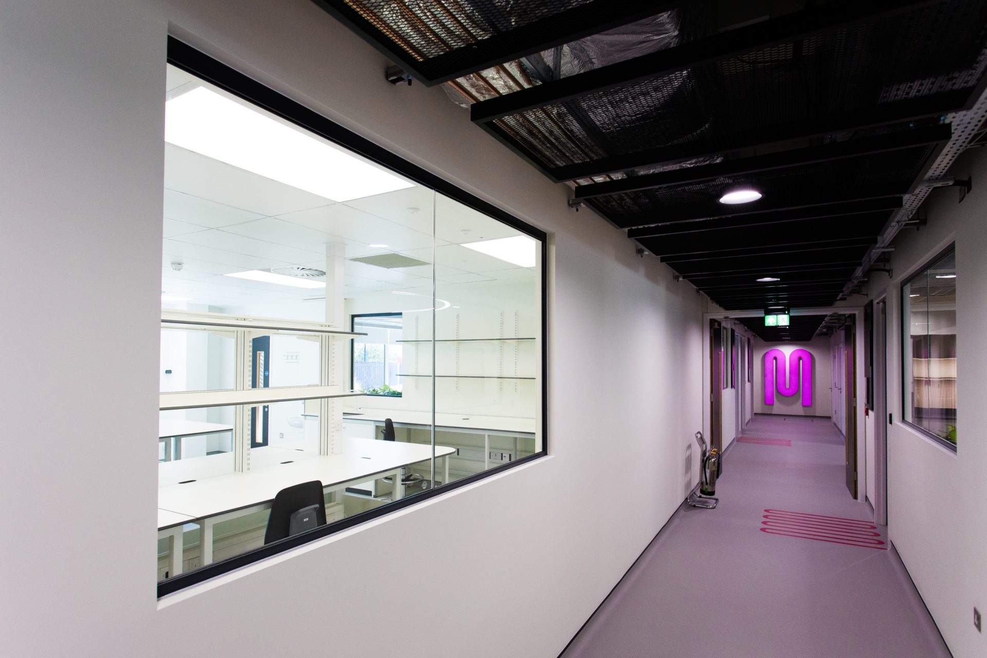 Modern office corridor with glass meeting rooms and a glowing pink wall logo