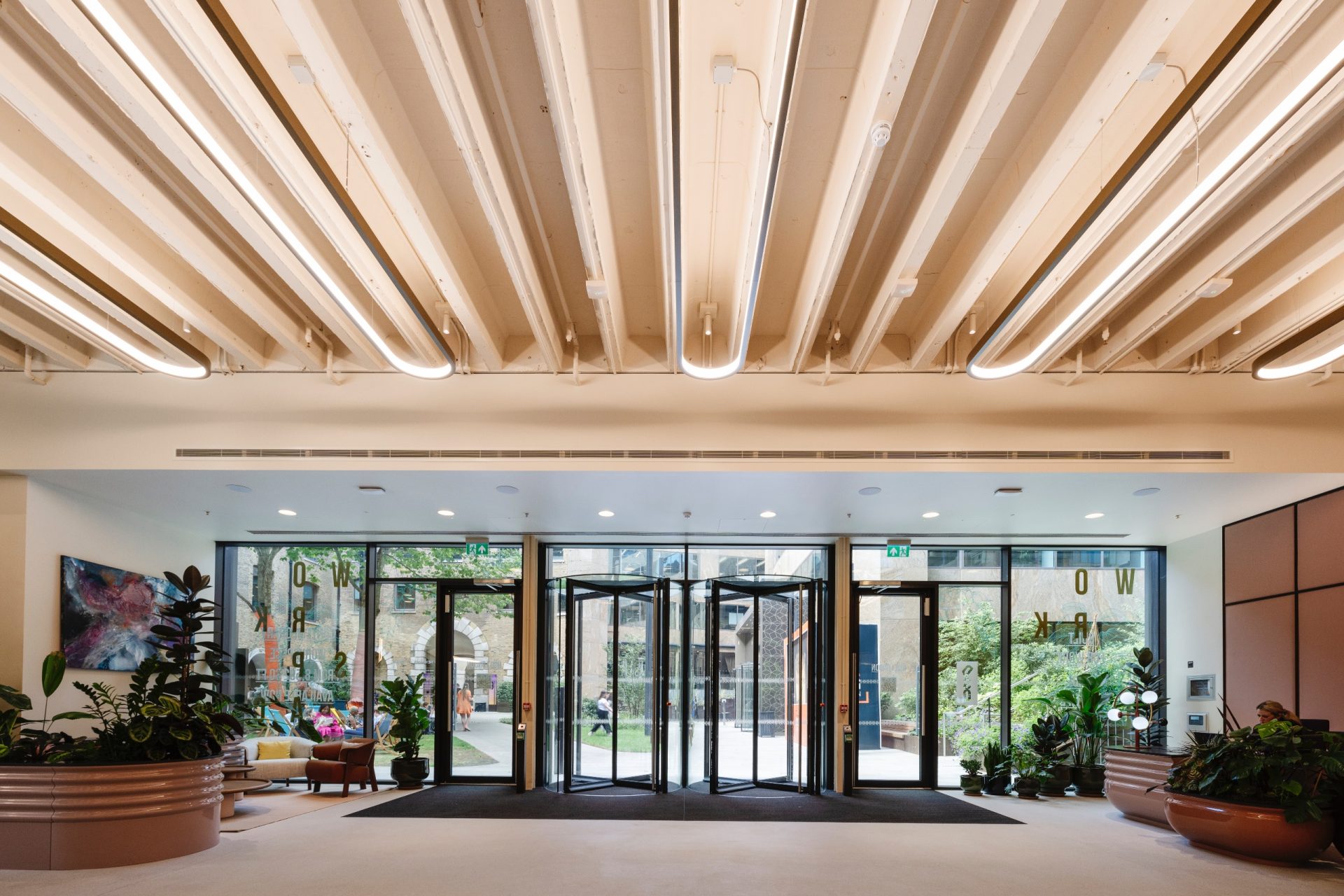 Modern commercial building lobby with glazed entrance doors, plants and exposed services ceiling