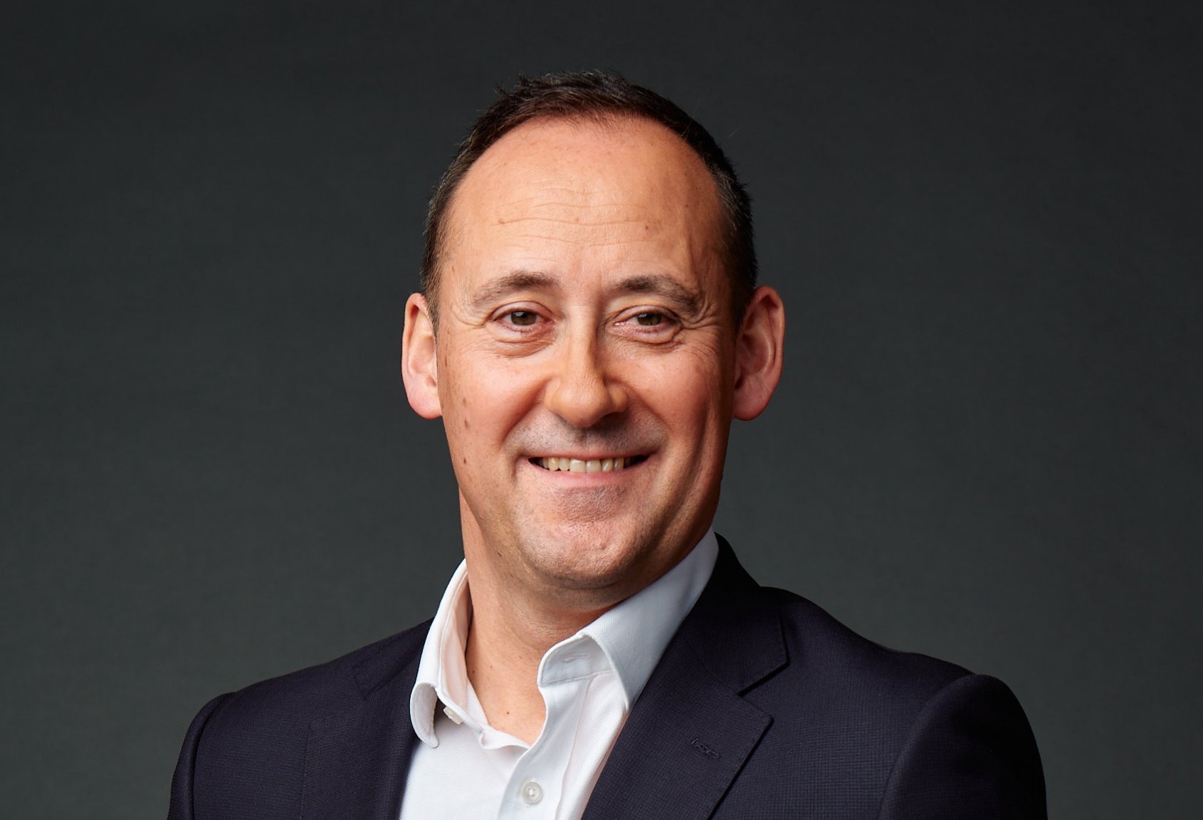 A smiling man wearing a dark suit jacket and white shirt