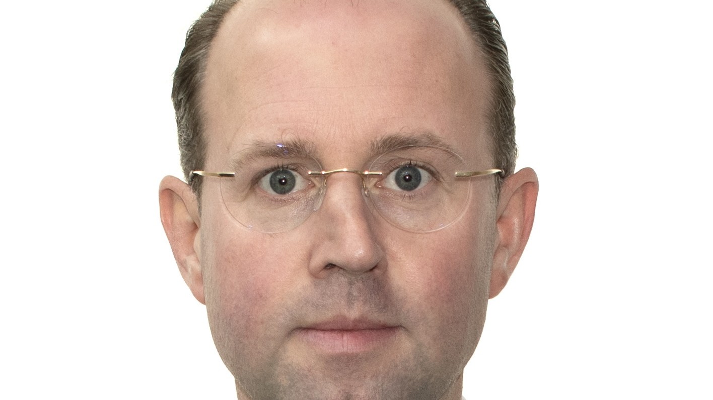 Professional man wearing glasses, a dark suit and blue tie against a white background