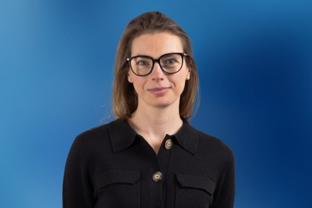 Louise Evans wearing glasses and a black shirt against a blue background.