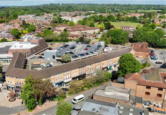 Aerial view of Oakdene Parade, with shops, flats above, parking and greenery.