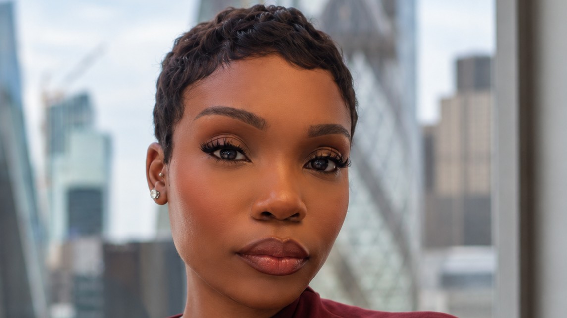 Amelie Ngombo, a project manager at AECOM, in a burgundy top against a blurred city skyline.