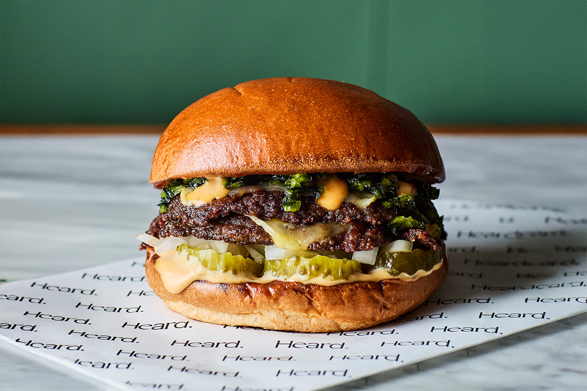 A hamburger sits on a surface printed with the Heard logo.