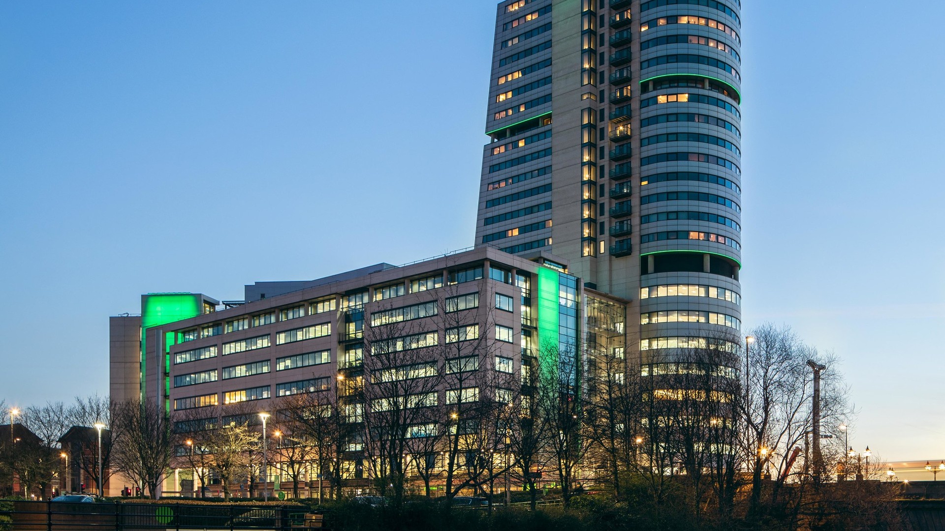Illustration of a modern high-rise office tower and adjoining commercial building at dusk