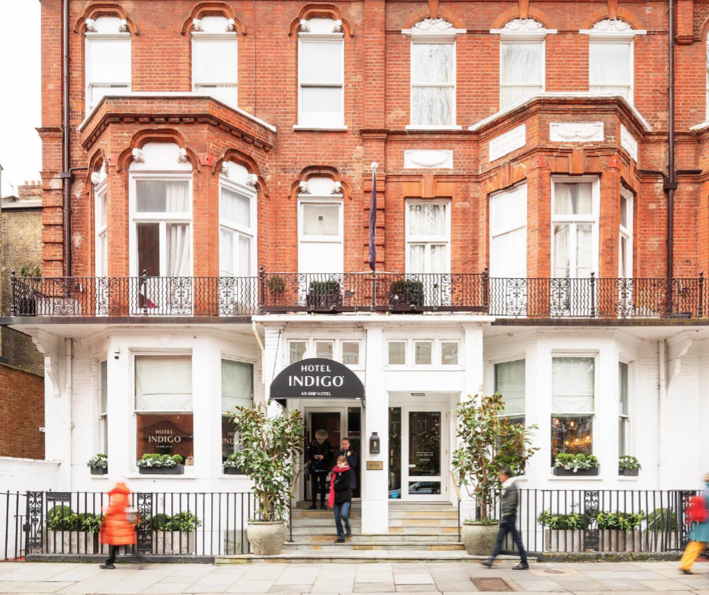Illustration of a Hotel Indigo entrance beneath a red-brick building, with pedestrians on the pavement.