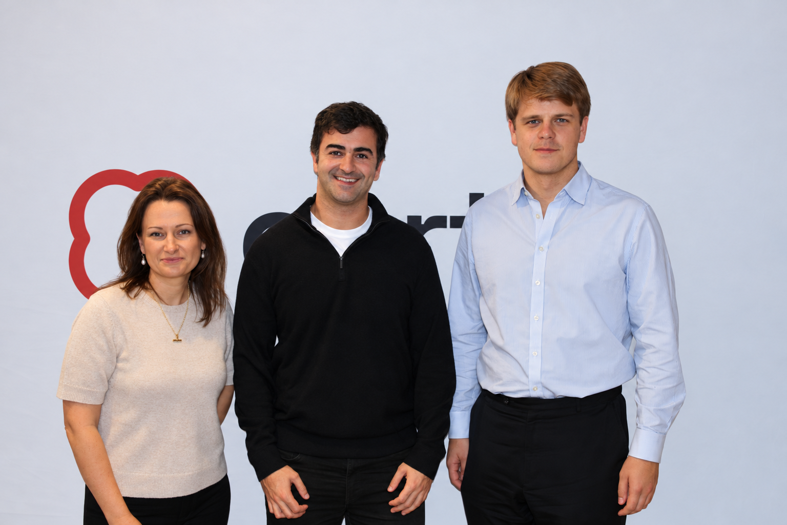 Three professionals stand side by side in front of a pale backdrop with a partially visible logo.