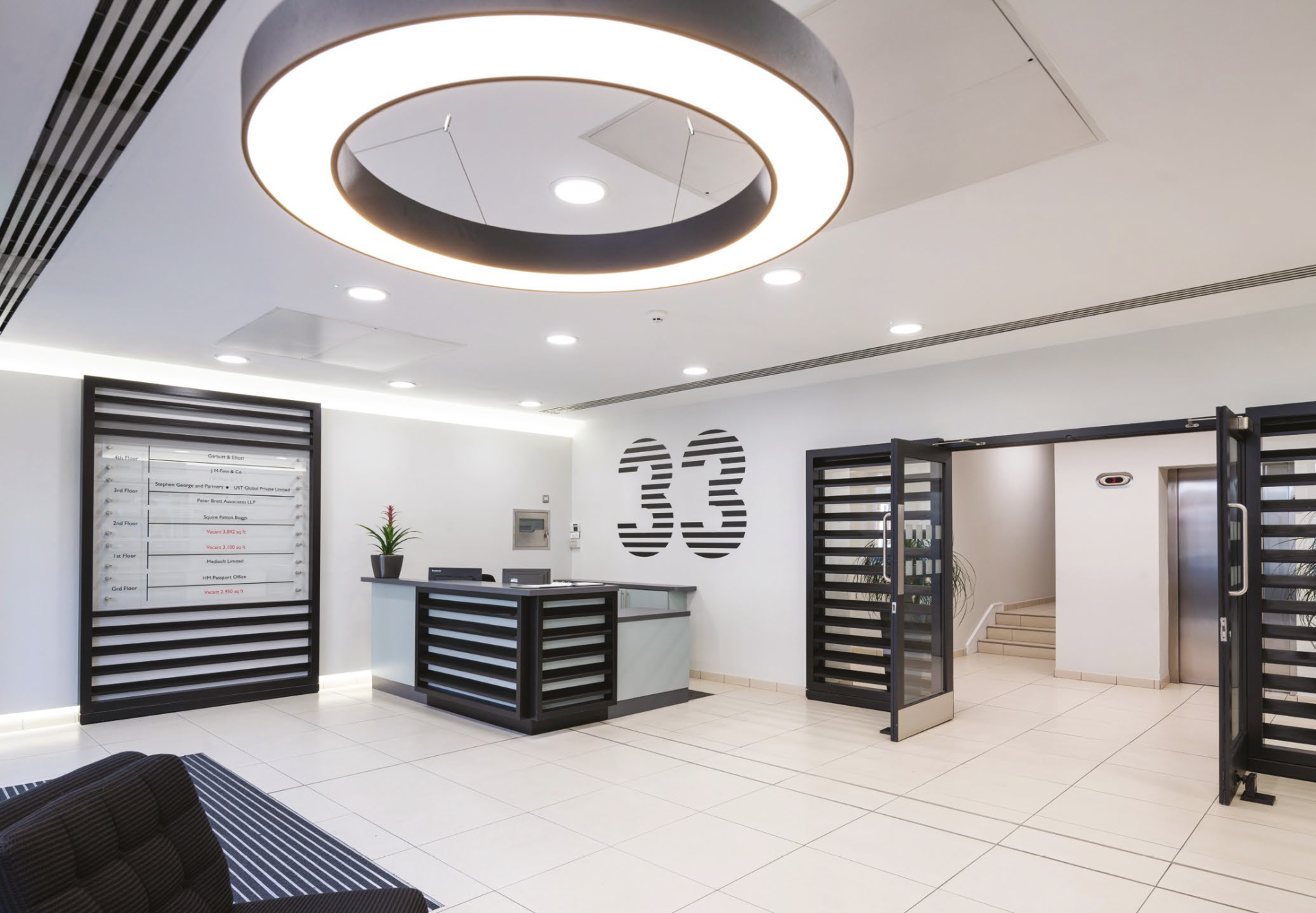 Modern commercial property reception with a reception desk, glass doors and a large circular ceiling light
