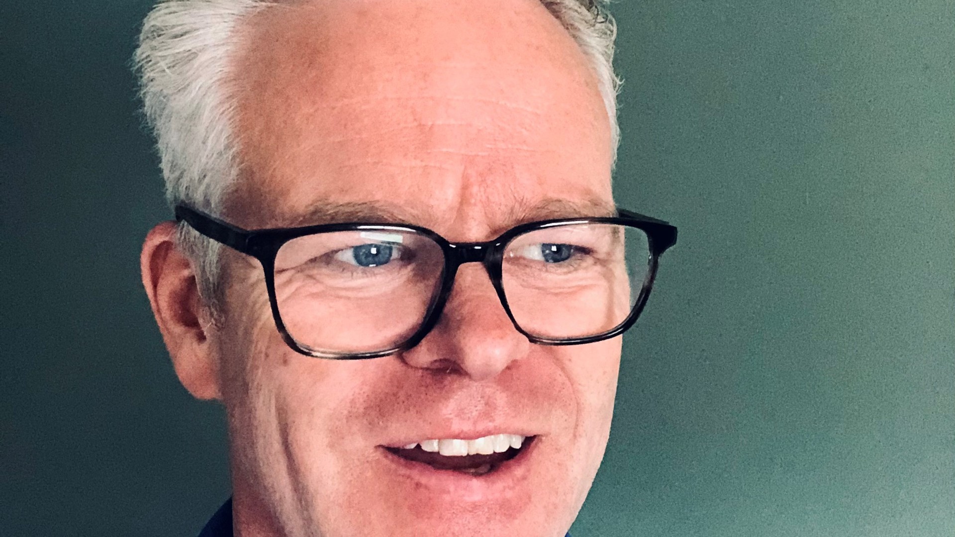 Andrew Stanford, a man with short gray hair and black glasses, smiles at the camera.