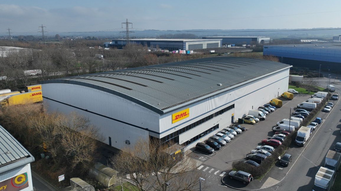 Aerial view of a large logistics warehouse and its car park, with rows of parked vehicles.