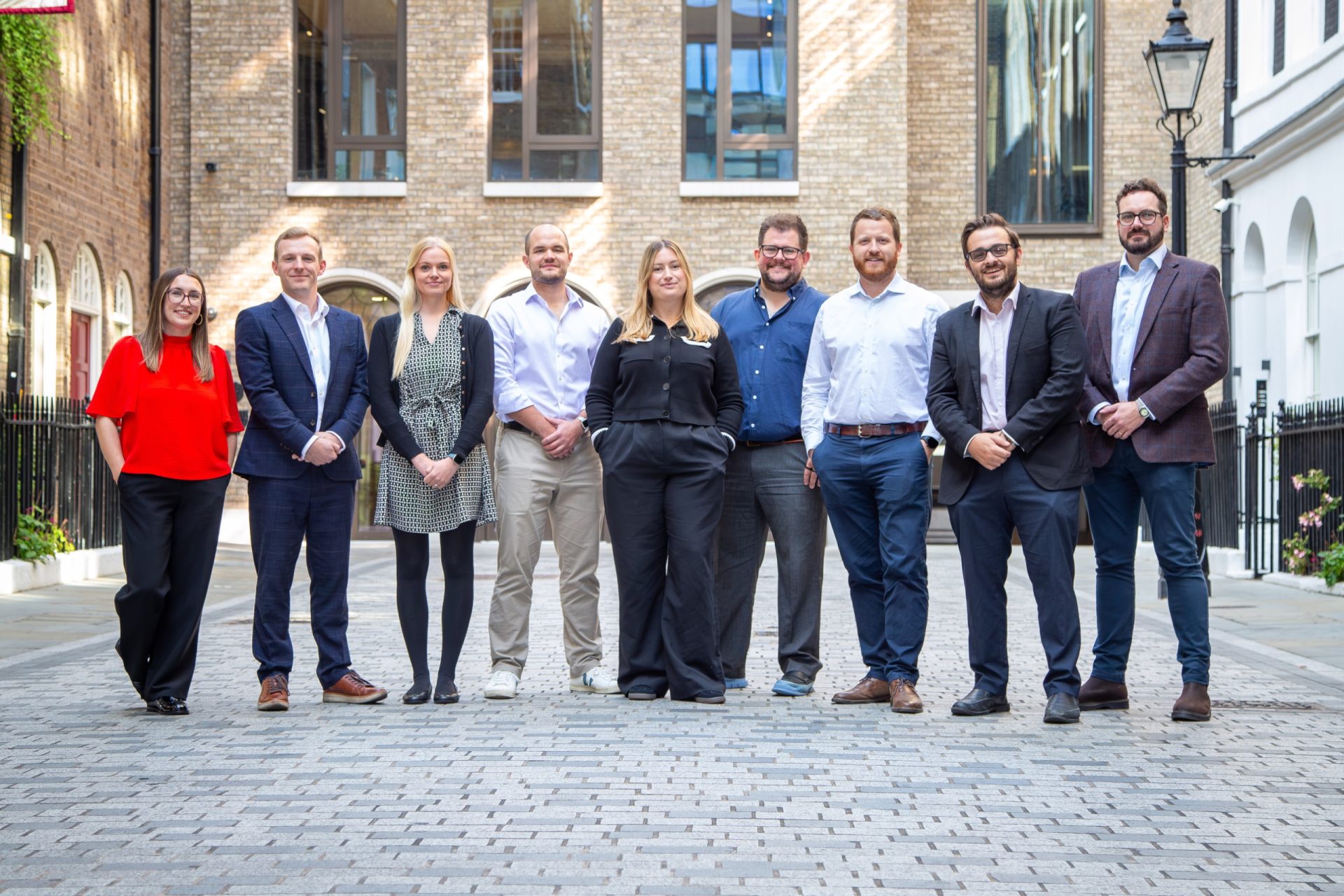 Nine property professionals pose together in a cobbled courtyard outside a brick office building.
