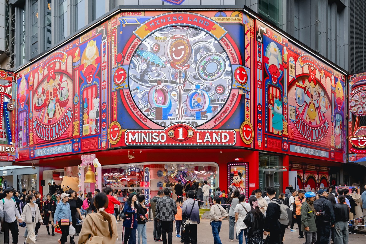 A crowd passes the brightly colored MINISO LAND storefront, with cartoon characters and themed displays across its facade.
