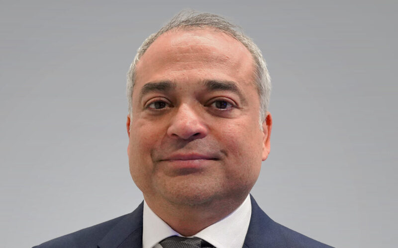 A smiling man with short grey hair wearing a blue suit jacket and a white shirt with a tie