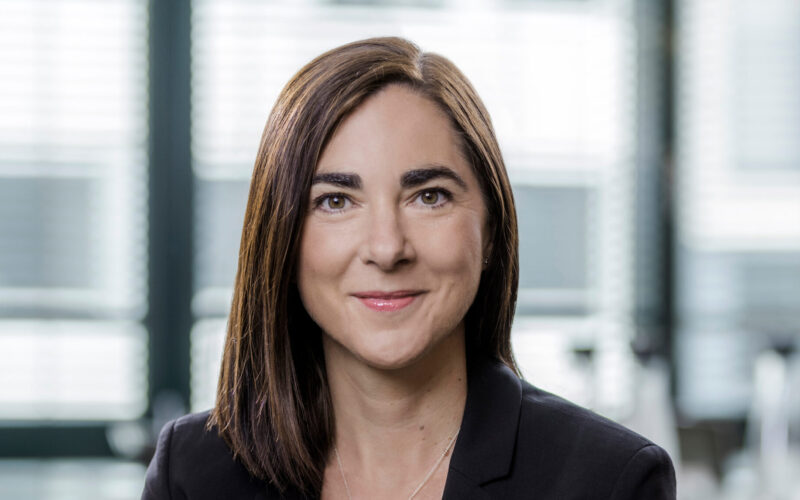 A smiling woman with long brown hair wearing a dark jacket