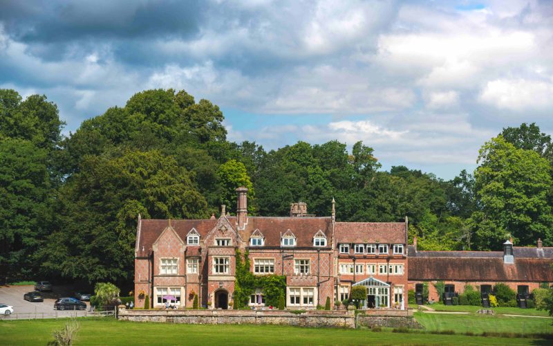 A grand old manor house with a lawn in the foreground and a wooded area behind