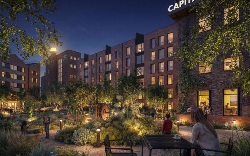 Image of a series of brick built buildings at night with a garden and seating in the foreground