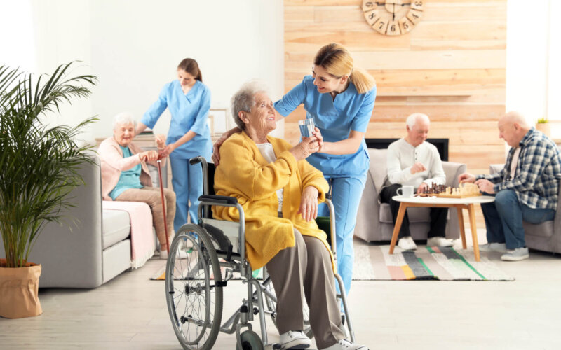 Nurse,Giving,Glass,Of,Water,To,Elderly,Woman,In,Wheelchair