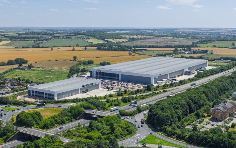 Aerial view of two large industrial buildings surrounded by roads and fields