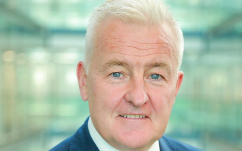 A grey haired man wearing a dark blue suit and tie and a white shirt