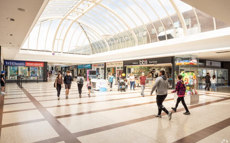 Interior of a shopping centre featuring lots of retail stores and shoppers