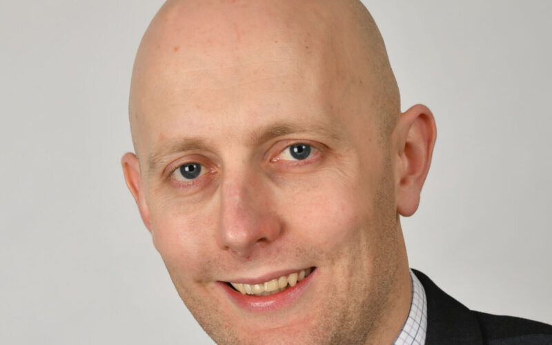 A smiling bald man wearing a suit jacket and collared shirt