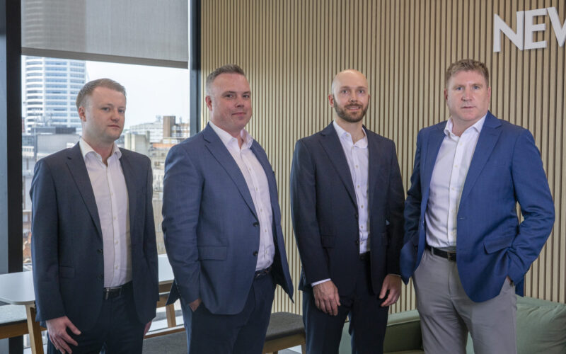 Four white males wearing suits stood in an office