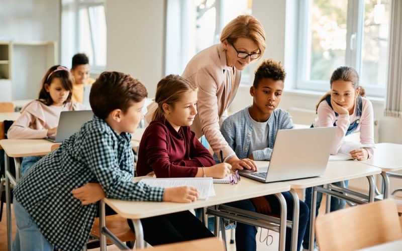 Elementary,Teacher,And,Her,Students,Using,Laptop,During,Computer,Class