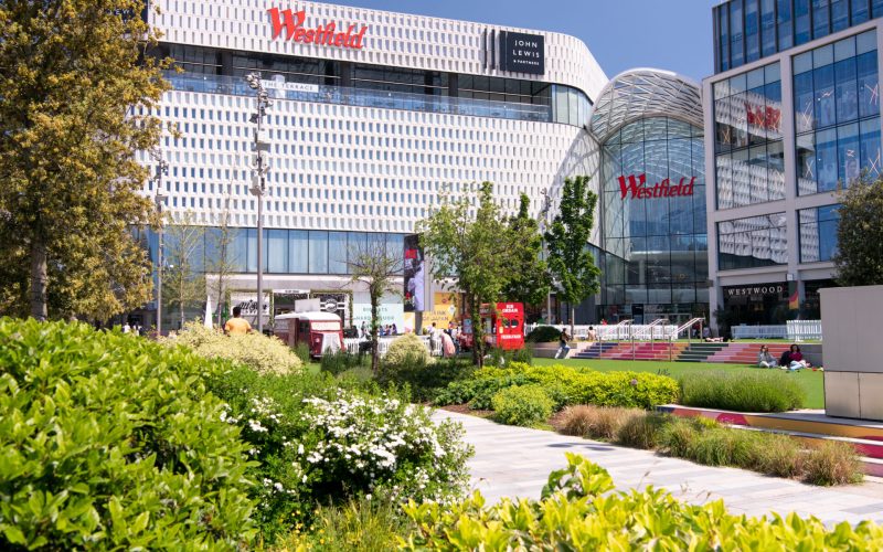 Exterior of a shopping centre bearing the logo 'Westfield' with green space in front