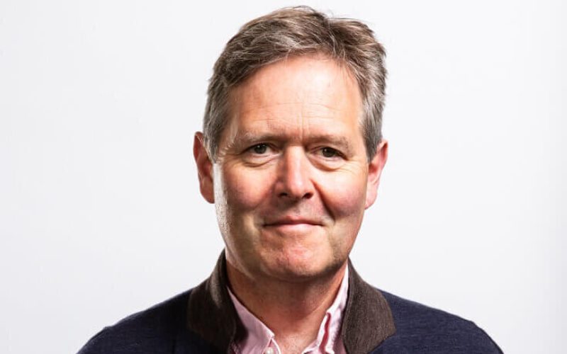 A white man wearing a dark jacket and a light shirt