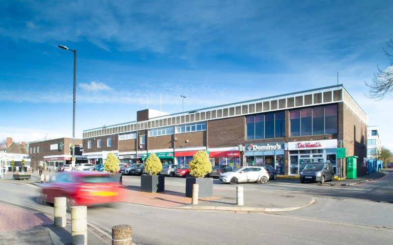 A shopping parade featuring a row of retail units with a main road in front