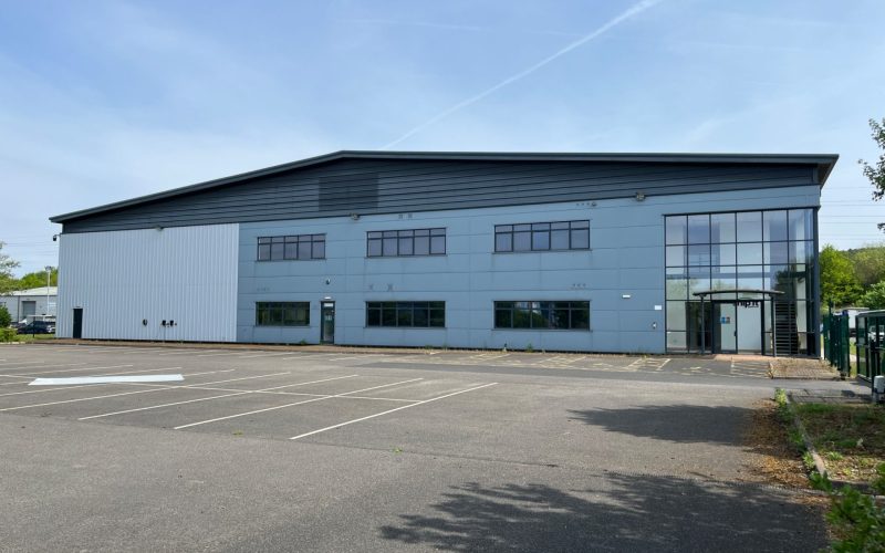 Blue industrial warehouse at Millennium Business Park, with office windows and a large car park in front.